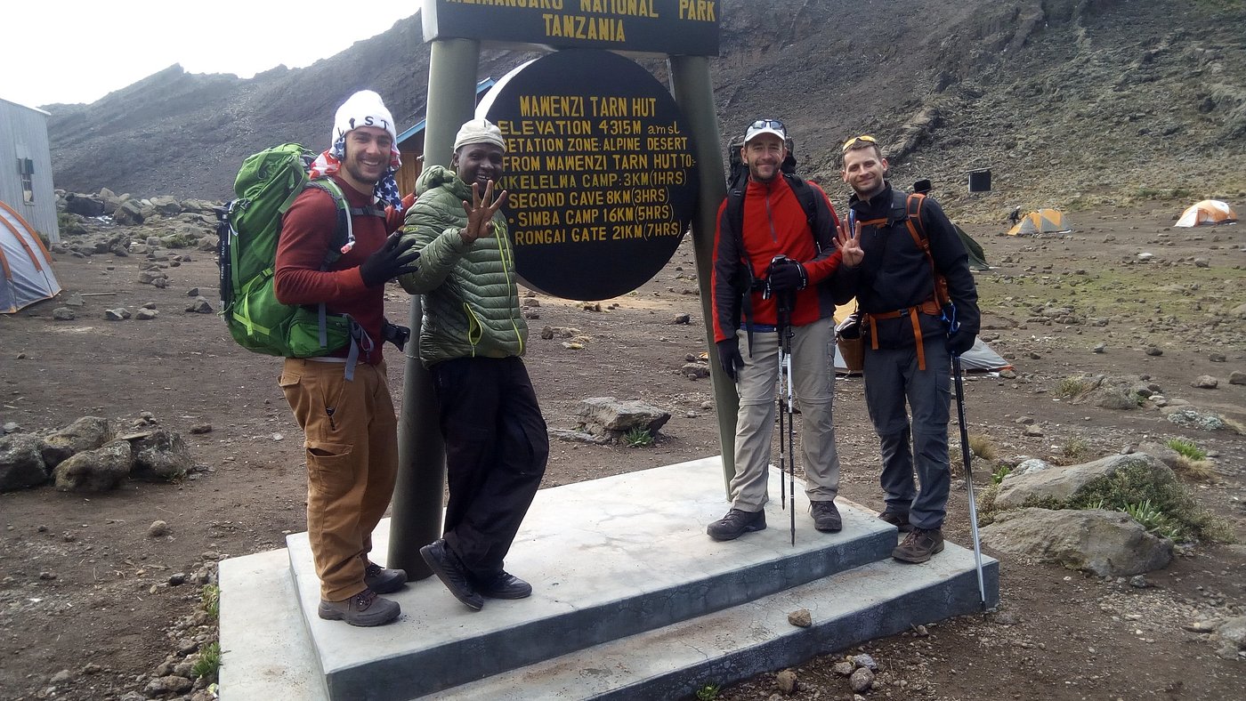 Kilimanjaro Success Rate by Route: Real Data From 1,247 Guided Climbs. | Kilimania Adventure Senior Kilimanjaro guide Sabinus Msimba with climbers at Mawenzi Tarn Hut Camp on the 7-day Rongai Route, a key acclimatization stop that improves Kilimanjaro summit success rates."Kilimanjaro Success Rate by Route",