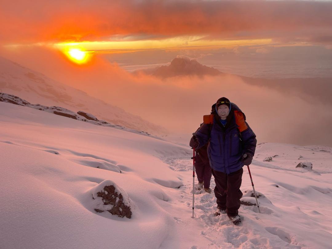Climbers crossing fresh snow near Uhuru Peak (5,895m) at golden sunrise — Mount Kilimanjaro summit morning