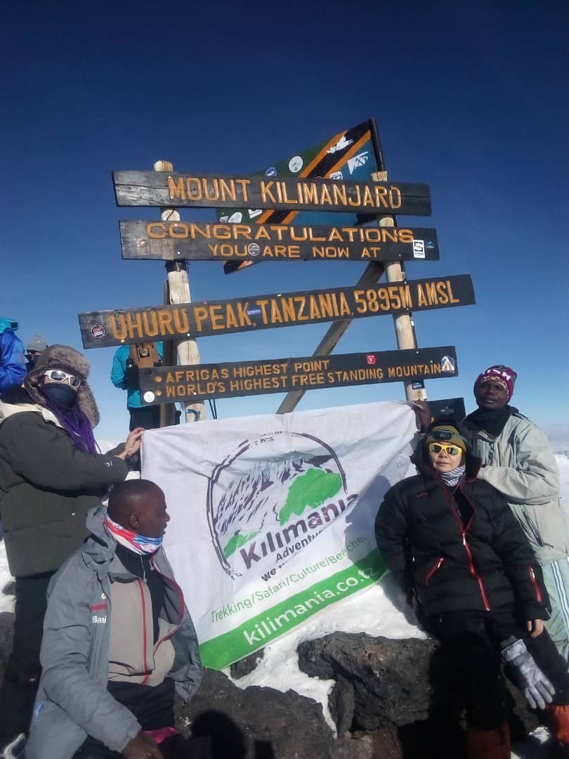 Sabinus Msimba with climbers at Uhuru Peak (5,895m), Mount Kilimanjaro summit, Tanzania, after completing the challenging summit night ascent at sunrise, worst part of climbing Kilimanjaro