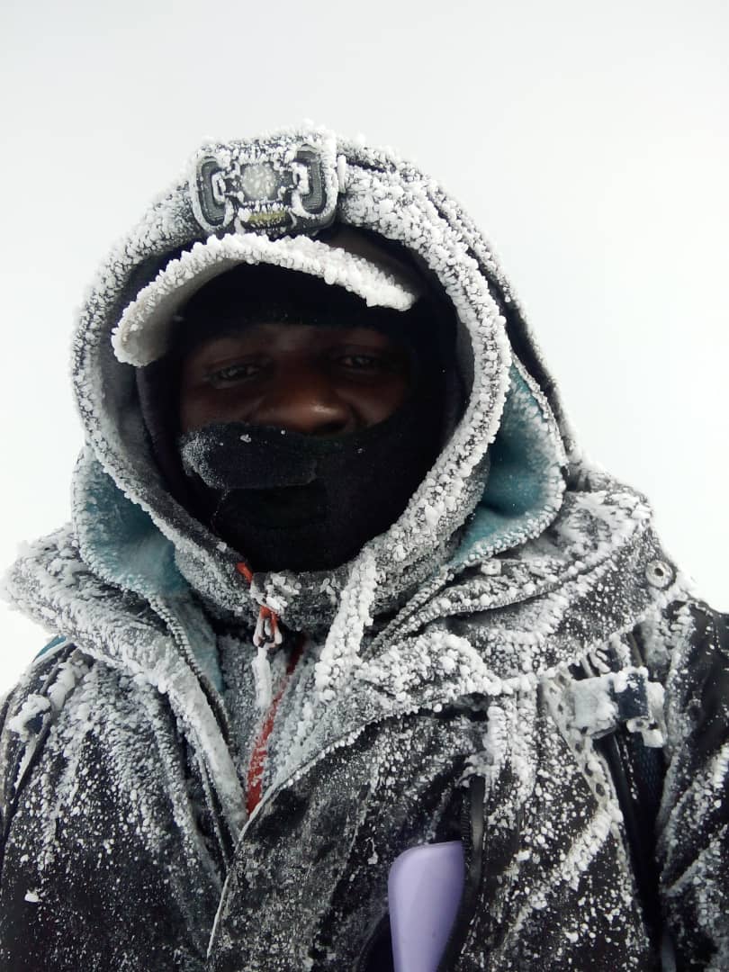 Senior Kilimanjaro Guide Sabinus Msimba standing at Uhuru Peak during heavy snowfall on Mount Kilimanjaro after ascending via the Umbwe Route.