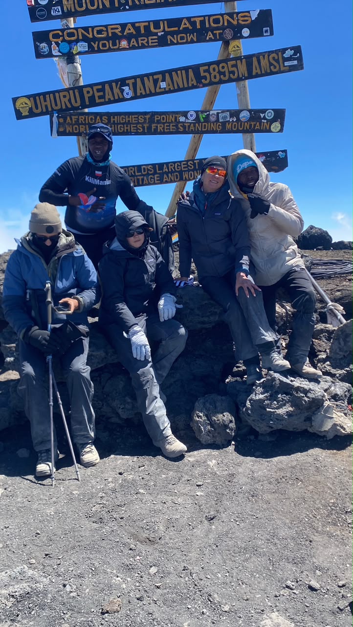 Senior Guide Sabinus Msimba celebrating a successful summit at Uhuru Peak with a family climbing team on the Lemosho Route