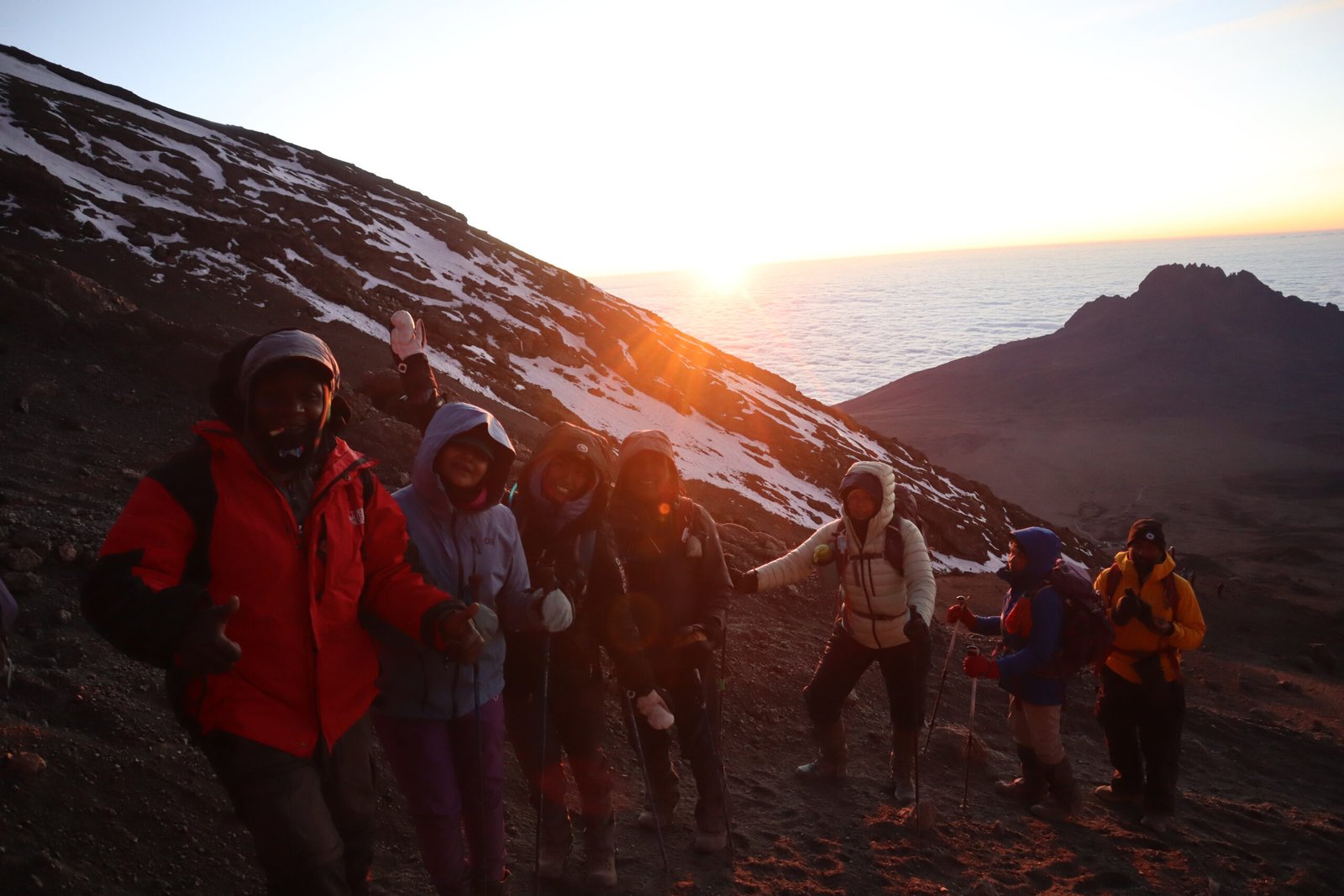 Senior Kilimanjaro guide Sabinus Msimba in red jacket leading climbers at sunrise near Stella Point on Mount Kilimanjaro summit night, Tanzania, July 2026