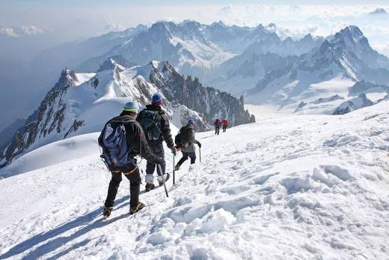 Mont Blanc glacier approach with climbers roped together on technical alpine terrain — crampons and ice axes required