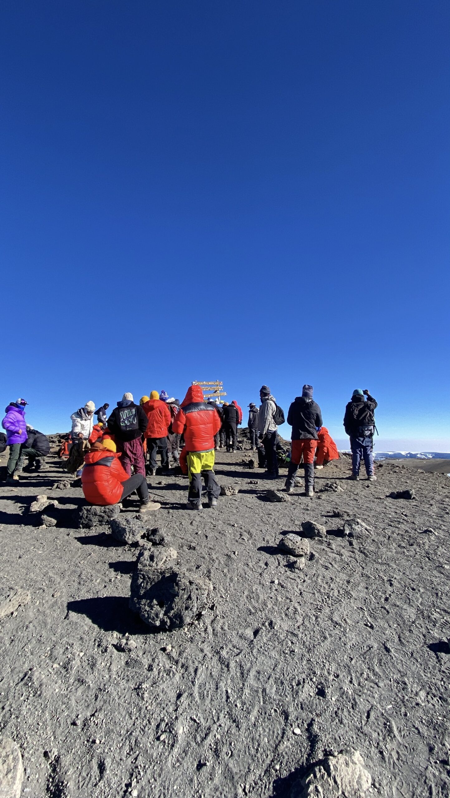 Climbers walking along the volcanic crater rim toward the Uhuru Peak summit sign on the Marangu Route
