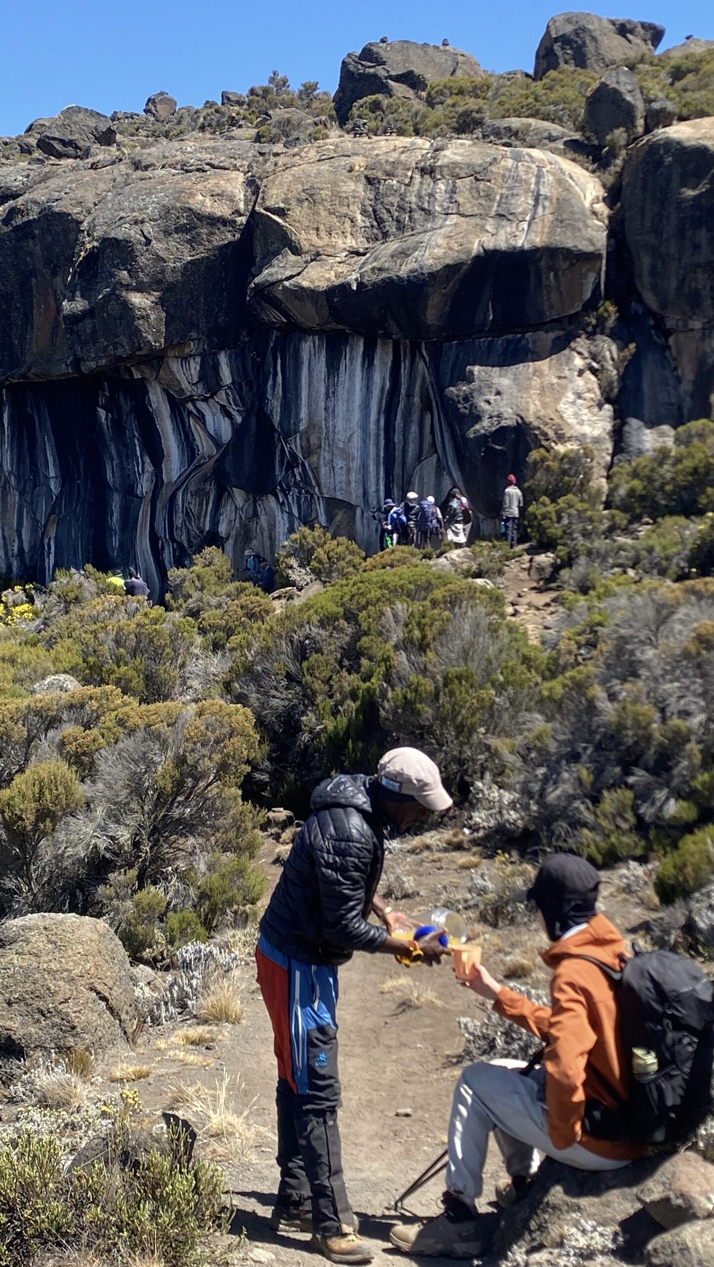 Kilimania support guide Peter serving a hot drink to a climber resting at the base of Zebra Rock