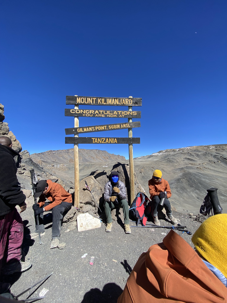 Climbers resting at Gilman's Point sign, 5,681 metres, on Mount Kilimanjaro's crater rim