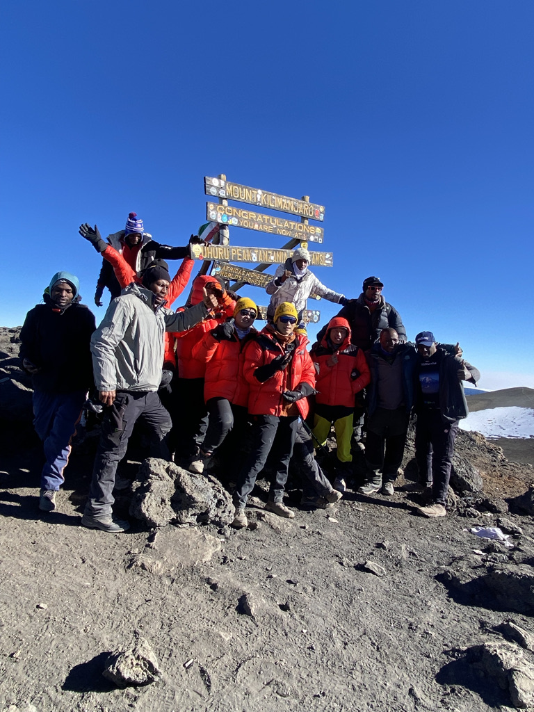 Climbers at the Uhuru Peak summit sign on Kilimanjaro at sunrise