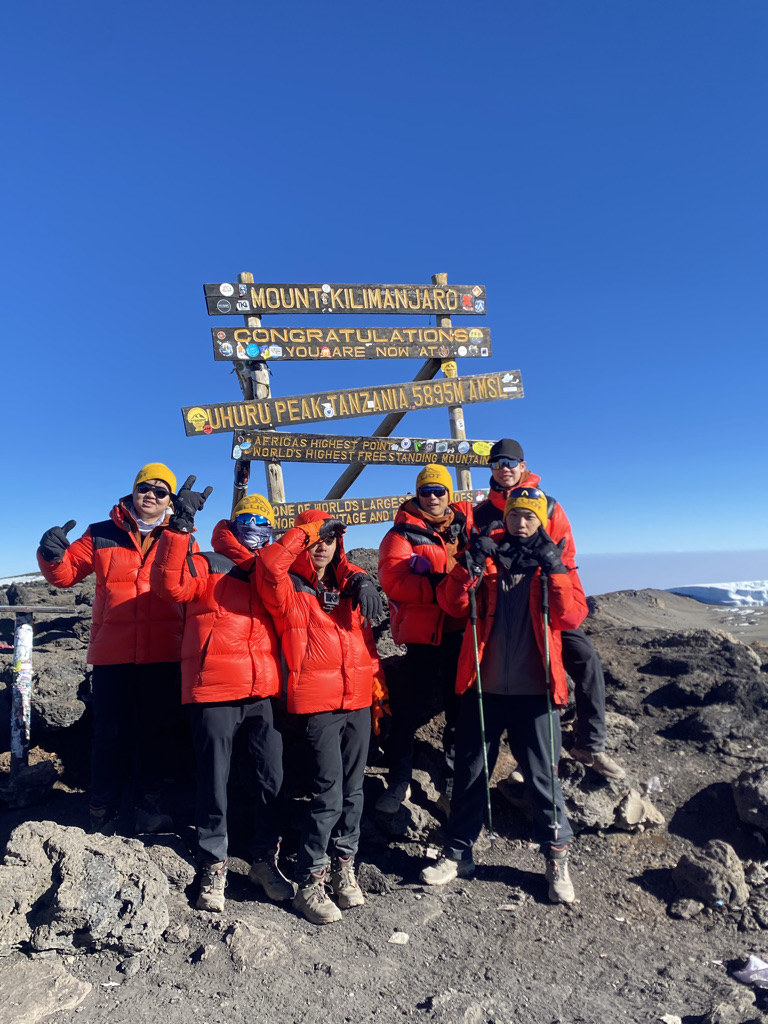 Climbers at Uhuru Peak, Kilimanjaro's summit sign, at 5,895 metres