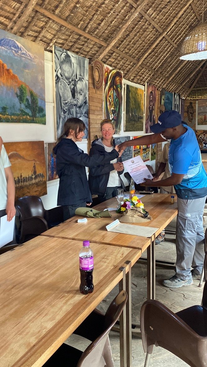 Senior Guide Sabinus Msimba presenting an official Kilimanjaro summit certificate to a successful climber in Moshi Tanzania