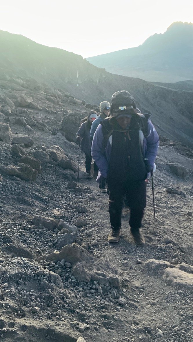 Senior Guide Sabinus Msimba leading a climbing group near Stella Point on Kilimanjaro during summit night — visible headlamps and pre-dawn darkness