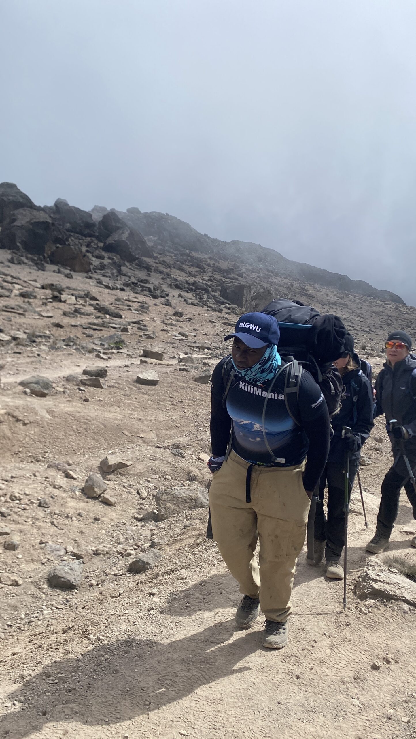 Senior guide Sabinus Msimba leading a Kilimania Adventure group across Kilimanjaro's volcanic scree