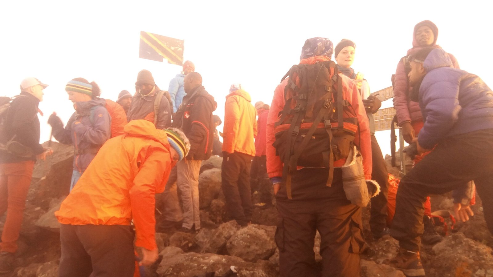 Climbers and guides at the Mount Meru summit area in dawn mist, a Tanzanian flag behind them