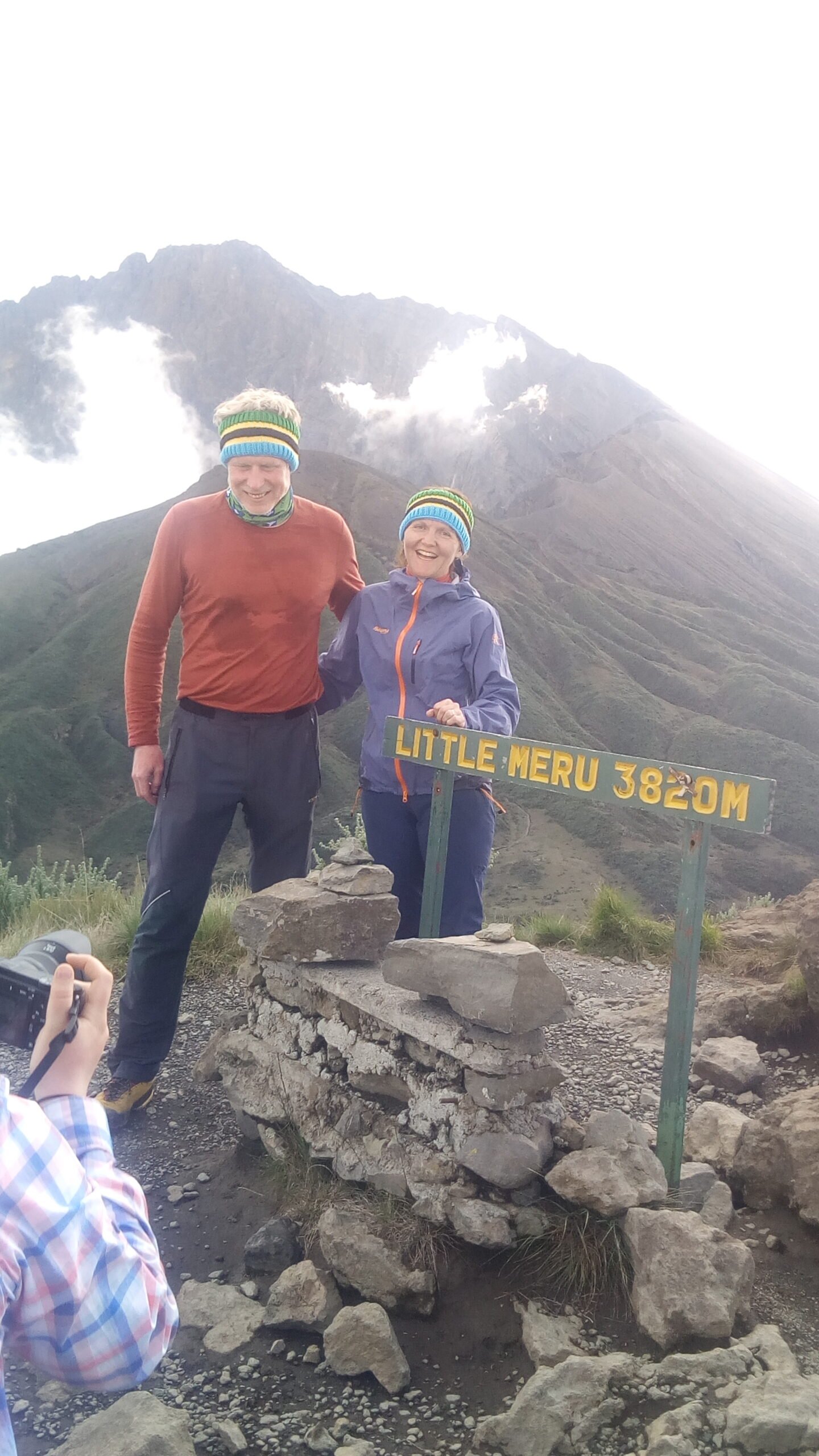 Two climbers at the Little Meru 3,820 m signpost with the Mount Meru cone rising behind them