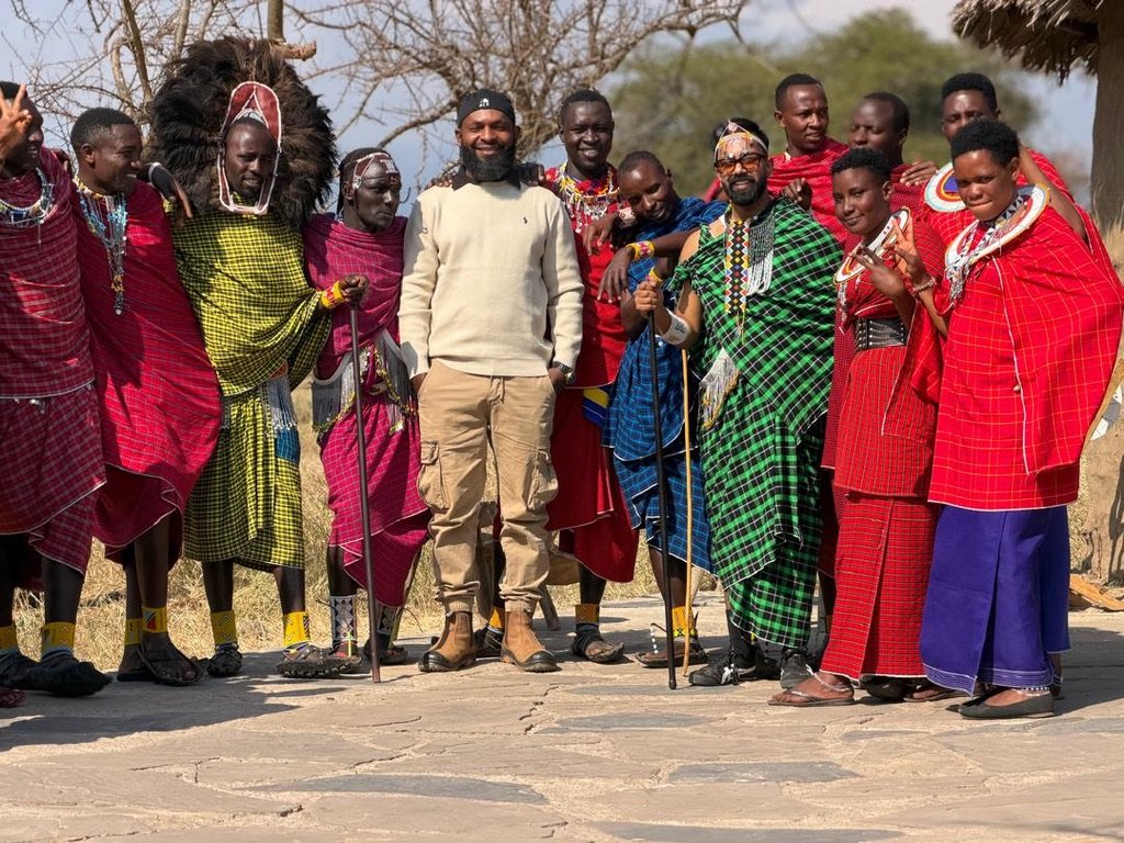 Kilimania guide in a cream jumper stands with Maasai men and women in red, green and blue shukas