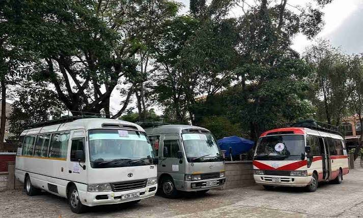 Three shared shuttle minibuses parked under trees, a common alternative to a private airport transfer in northern Tanzania