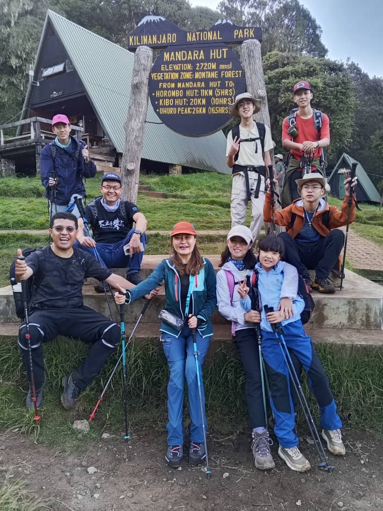 Family group with children and trekking poles at the Mandara Hut sign, 2,720 m, Kilimanjaro National Park