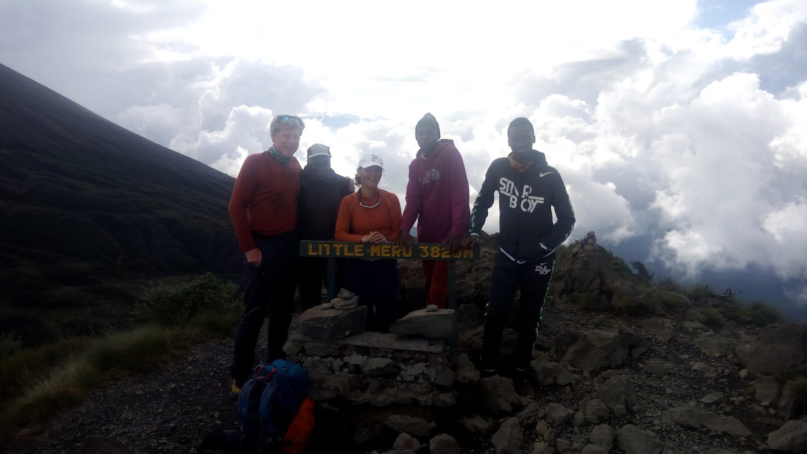 Sabinus Msimba with climbers at the Little Meru signpost, cloud moving over the Mount Meru ridge
