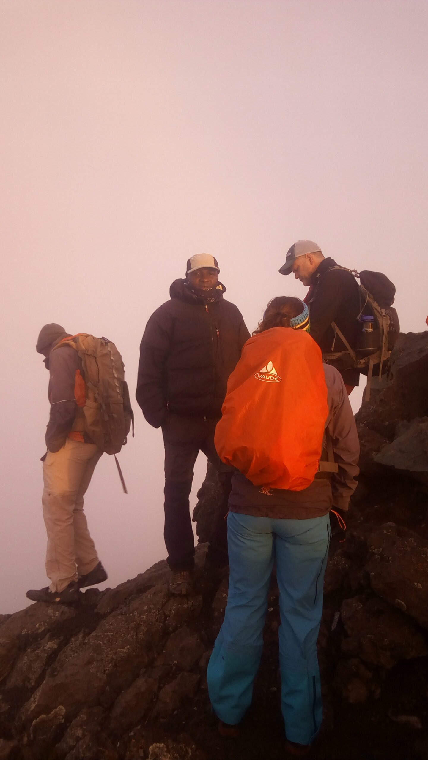 Climbers with backpacks on a rocky Mount Meru summit ridge in thick fog before sunrise