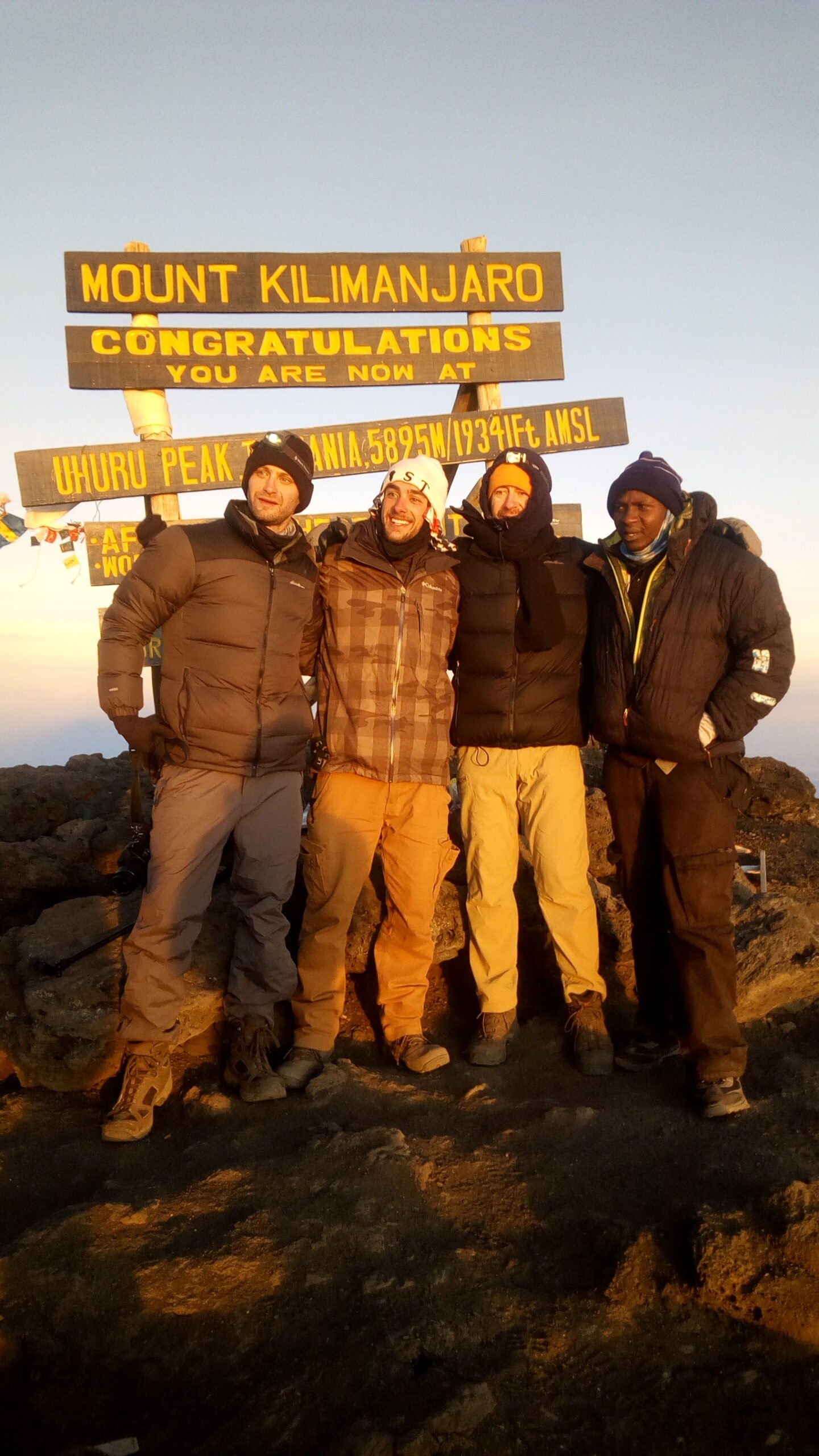 Sabinus Msimba and climbers at Uhuru Peak summit sign on the Rongai Route, Kilimanjaro